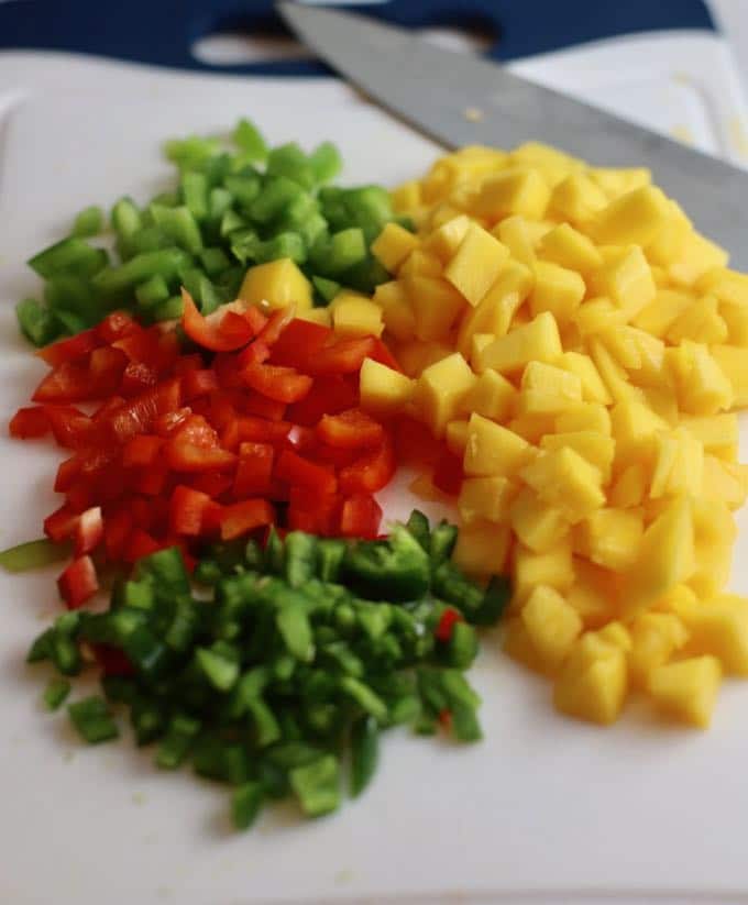 Chopped mango, red and green bell pepper and a jalapeño pepper on a cutting board.