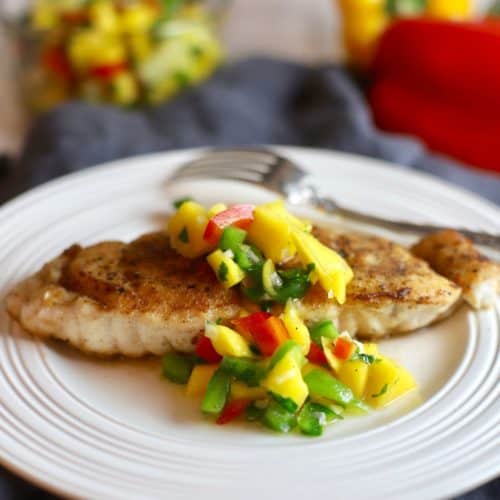 Pan Seared Red Snapper fillet covered with Mango Salsa on a white plate.