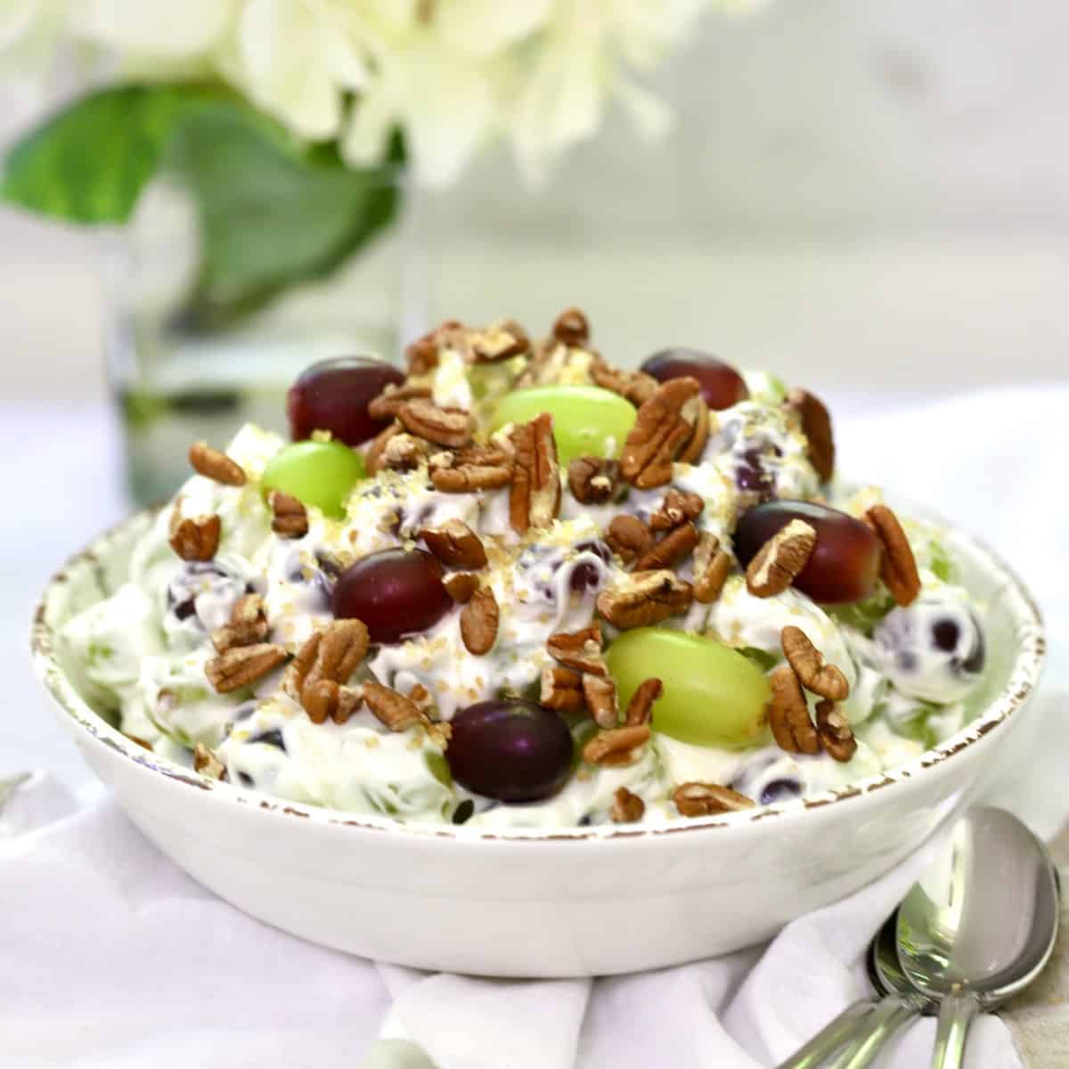 Easy Grape Salad with Cream Cheese in a white bowl garnished with pecans and with hydrangeas in the background