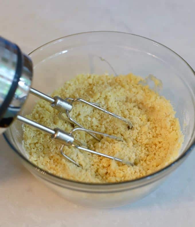 A clear glass bowl with eggs, sugar and flour being mixed together with an electric mixer. 