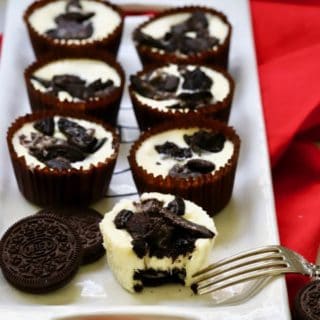 Seven Oreo cheesecake cupcakes on a white serving dish with a fork.