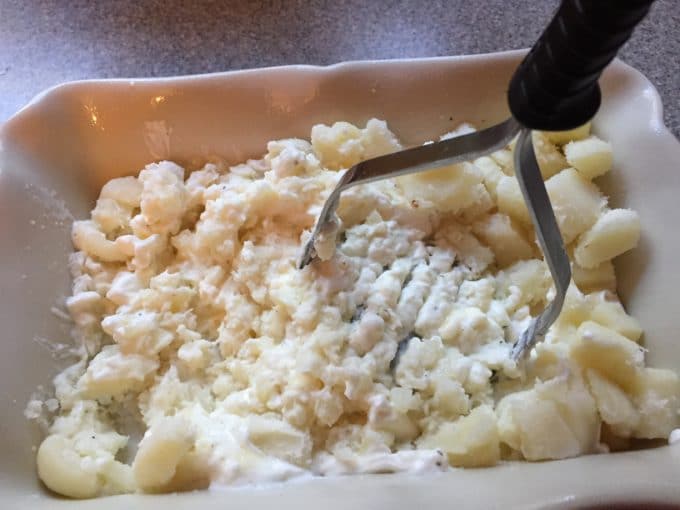 Mashing potatoes in a dish with a potato masher. 