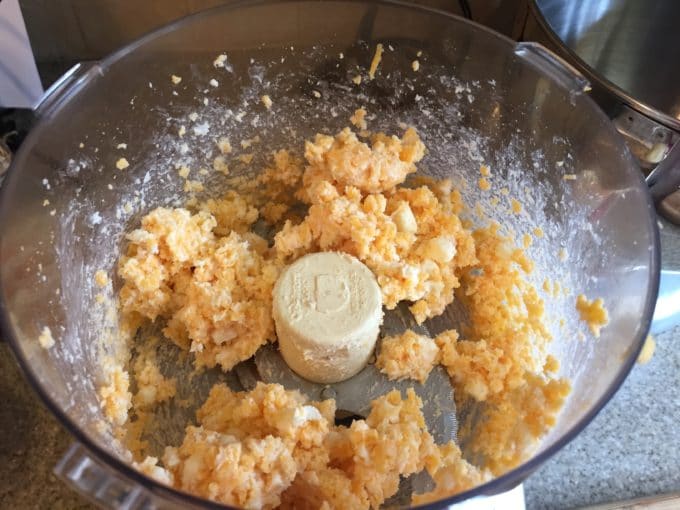 Shredded cheese and butter in the bowl of a food processor.