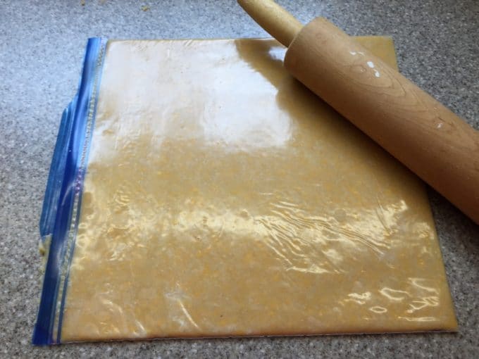 A Ziplock storage bag full of cheese cracker dough rolled flat with a rolling pin.