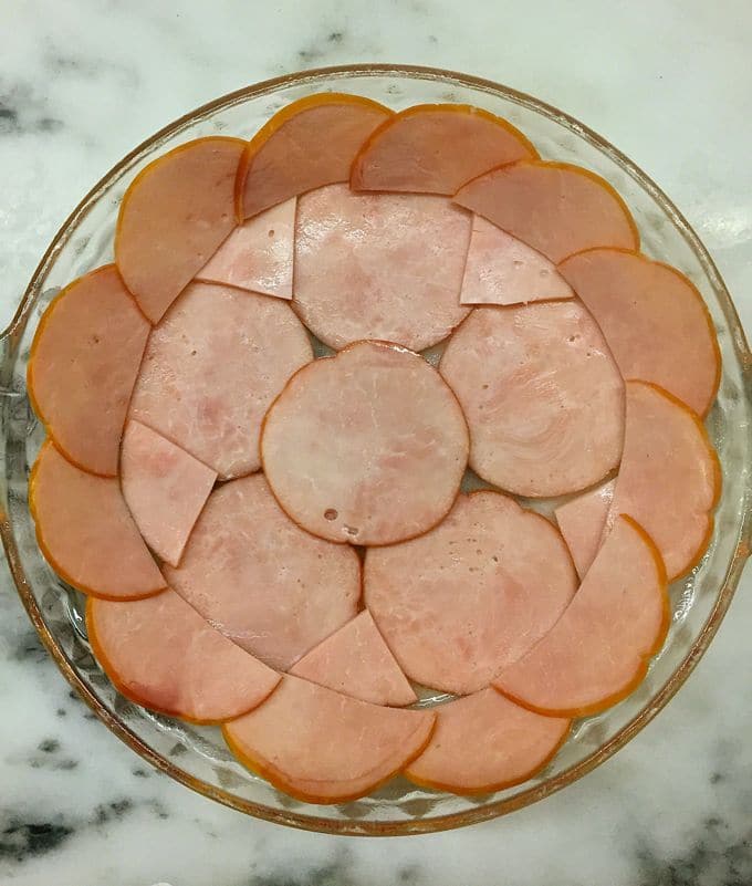 Canadian bacon covering the bottom and sides of a glass pie dish.