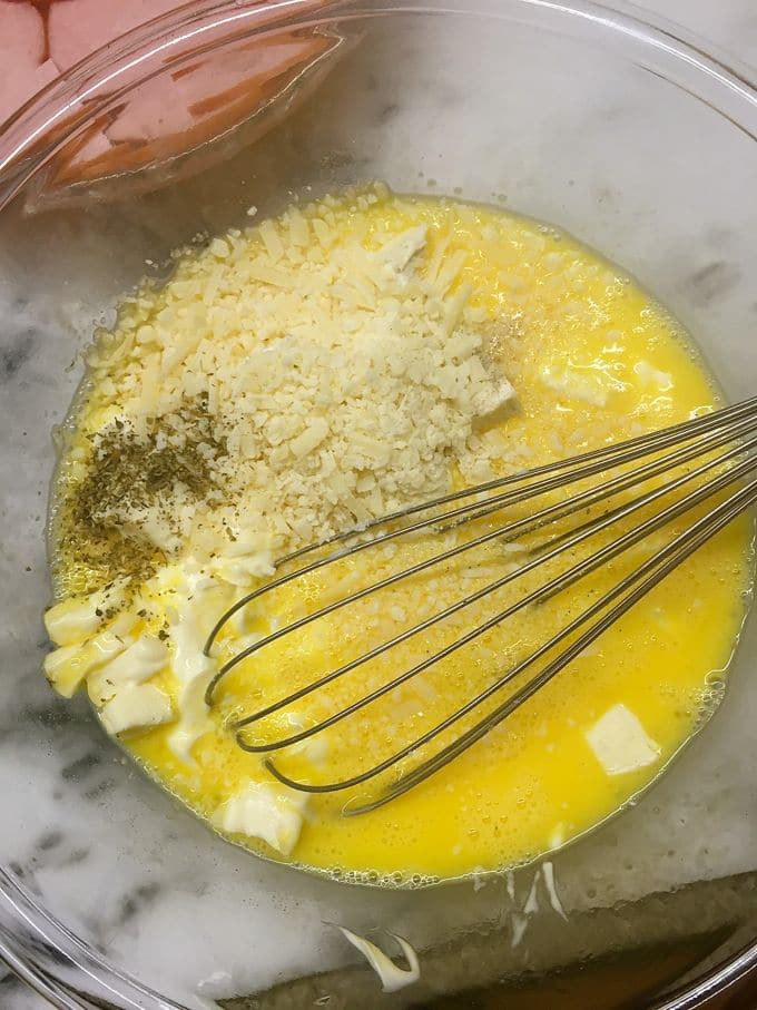 A glass bowl with eggs, cheese and seasonings to make a quiche. 
