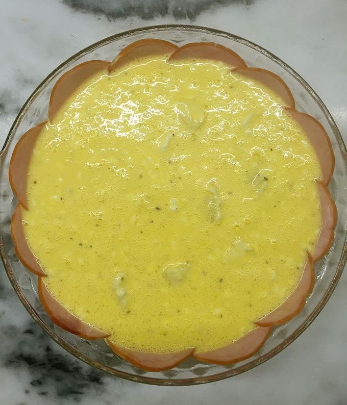A glass pie dish full quiche filling with Canadian bacon forming the crust. 