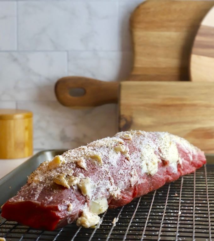 A beef tenderloin slathered in butter on a wire rack on a baking sheet. 