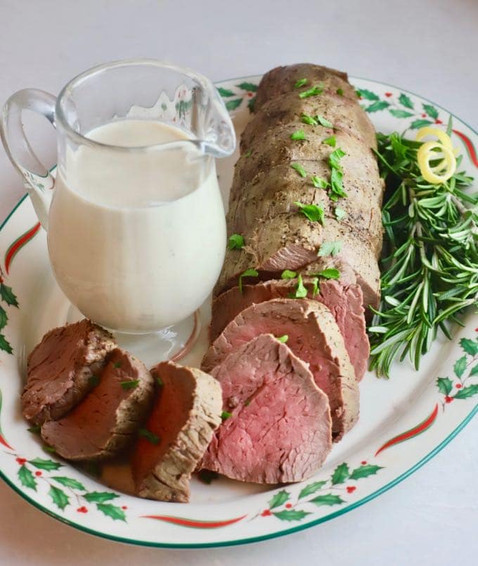 Roasted Beef Tenderloin on a Christmas plate with a small pitcher of onion sauce. .
