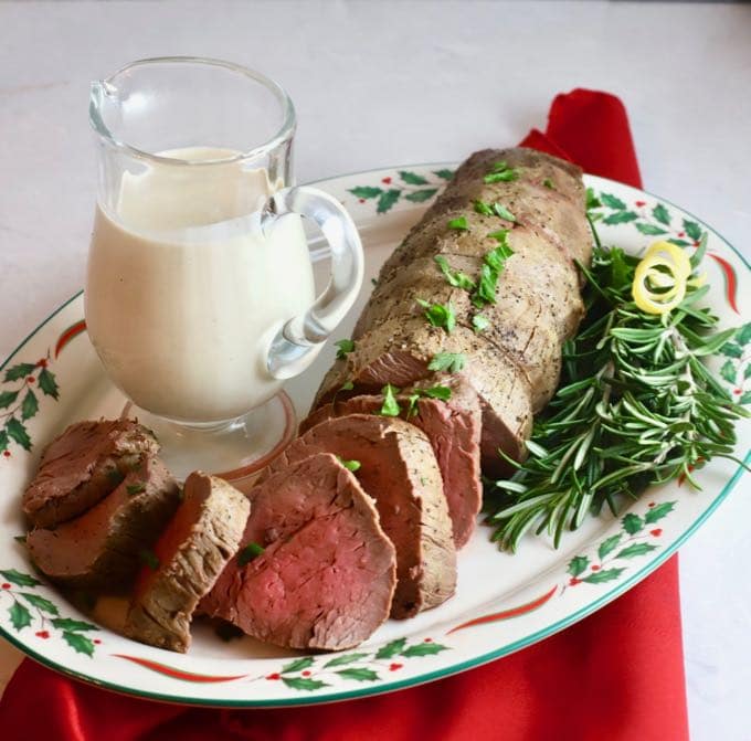 Roasted Beef Tenderloin with Onion Blue Cheese Sauce on a Christmas plate and red napkin.
