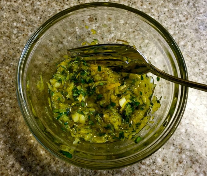 Mixed thyme, garlic, lemon zest and olive oil in a glass bowl.