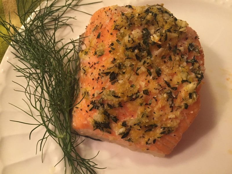 A piece of cooked salmon topped with herbs on a plate.