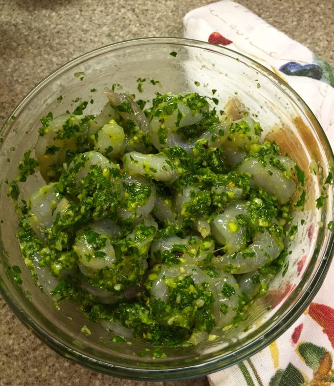 Shrimp marinating in a clear glass bowl in a sauce made with parsley and scallions for Spicy Shrimp and Green Sauce
