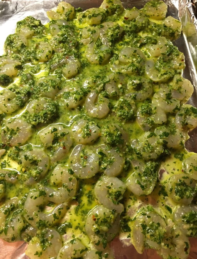 Shrimp on a baking sheet covered with a sauce made with parsley, olive oil, wine, and scallions for Spicy Shrimp with Green Sauce