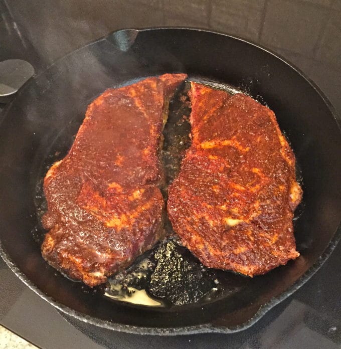Two ribeye steaks cooking in a hot cast-iron skillet.