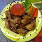 Baked Buffalo Wings on a yellow plate with a small bowl of buffalo sauce on the side.