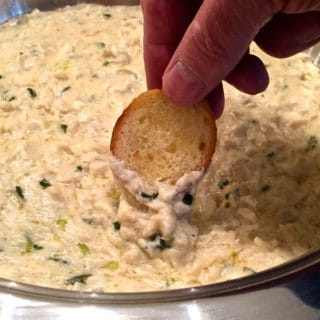 Dipping a toasted baguette slice into Easy Crab Mornay Dip