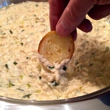 Dipping a toasted baguette slice into Easy Crab Mornay Dip