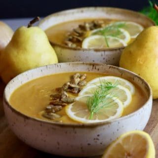 Two bowls of butternut pear squash soup topped with lemon slices and fennel.