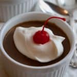 Two white bowls full of chocolate pudding topped with whipped cream.