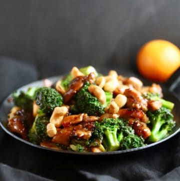A small black skillet full of chicken and broccoli stir fry topped with cashews.