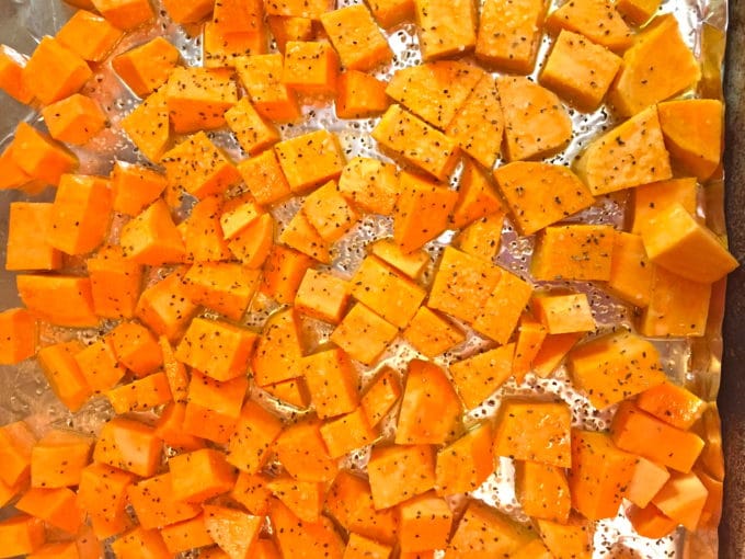 A layer of cubed sweet potatoes on a sheet pan ready for the oven.