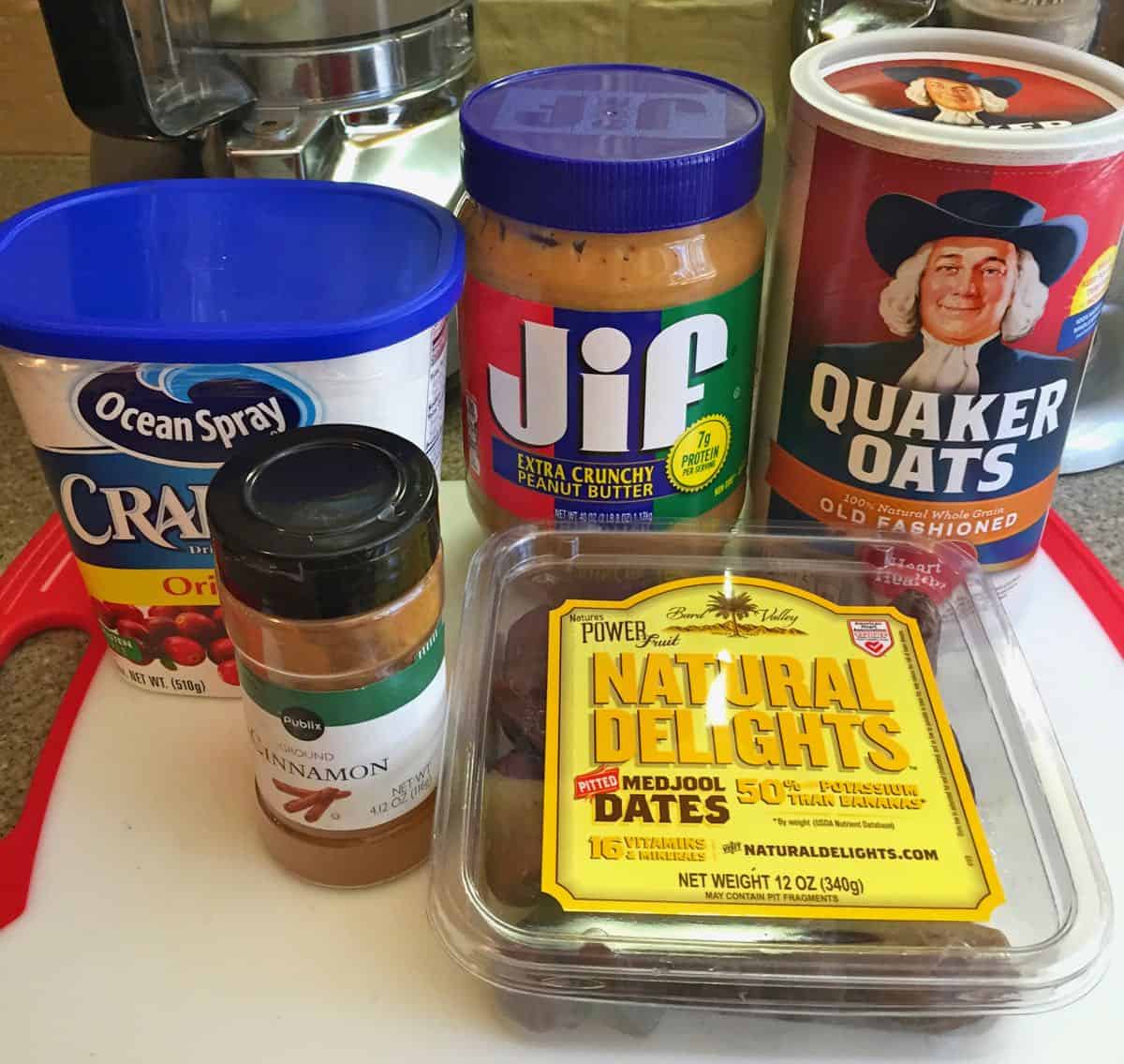 A box of oats, dates, Craisins, peanut butter, and cinnamon on a white cutting board. 