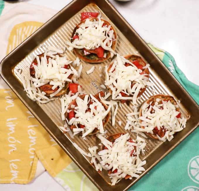 English muffin halves topped with mozzarella cheese on a baking sheet. 