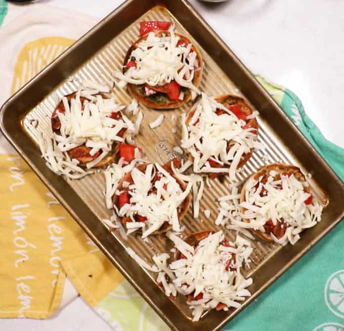 English muffin halves topped with mozzarella cheese on a baking sheet. 