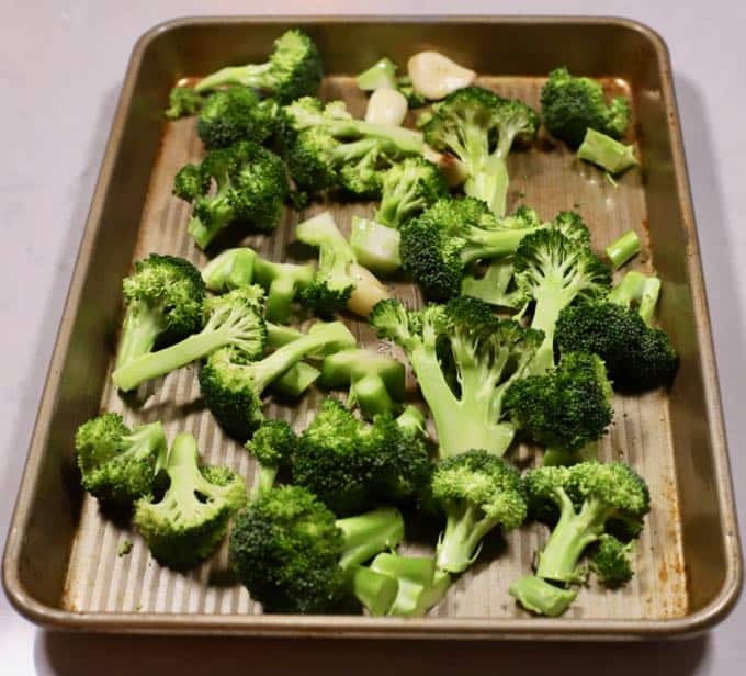 Broccoli florets and garlic gloves on a baking sheet.