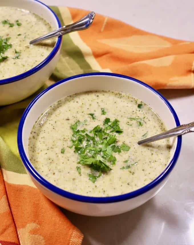 A bowl of white bean soup with broccoli on a green and orange kitchen towel.