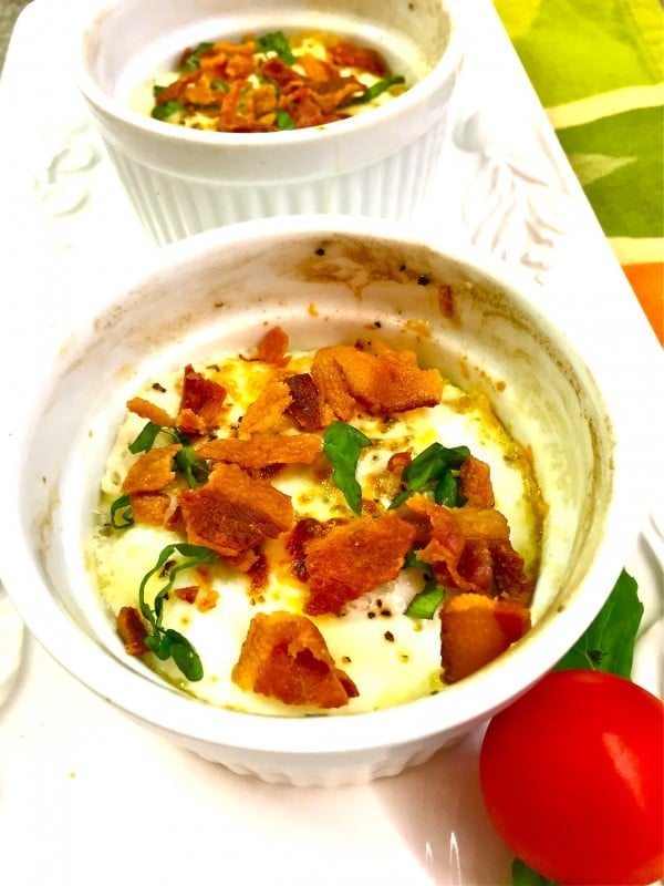 Two Baked Egg Cups garnished with bacon and basil on a white serving platter.