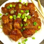 Sweet and sour chicken topped with chopped scallions on a white plate.