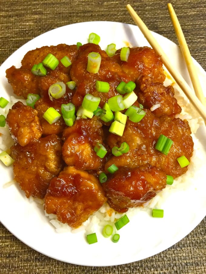 Easy Sweet and Sour Chicken over rice and topped with scallions on a white plate.