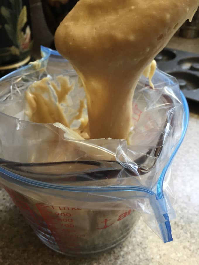 Using a spoon to drop donut batter into a storage bag.