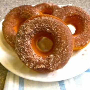 Four donuts covered in cinnamon sugar on a white plate.