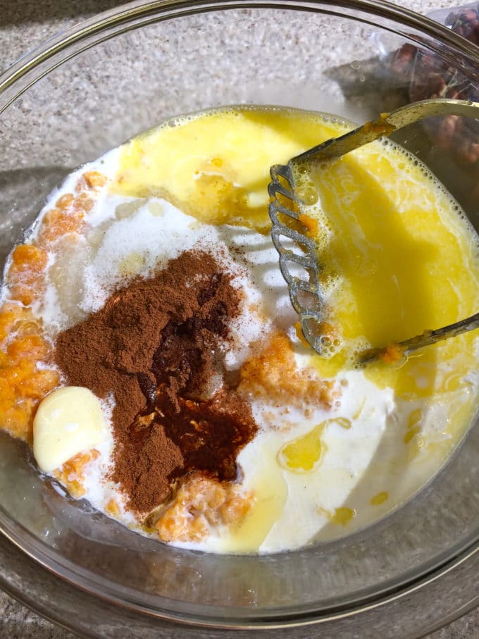 A clear glass bowl with eggs, brown sugar, cinnamon, butter and sweet potatoes. 