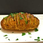 One Hasselback Potato cut in thin slices and garnished with parsley on a cutting board.
