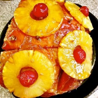 Brown Sugar Bourbon Glazed Ham in a cast iron skillet covered with pineapple slices, cloves and cherries