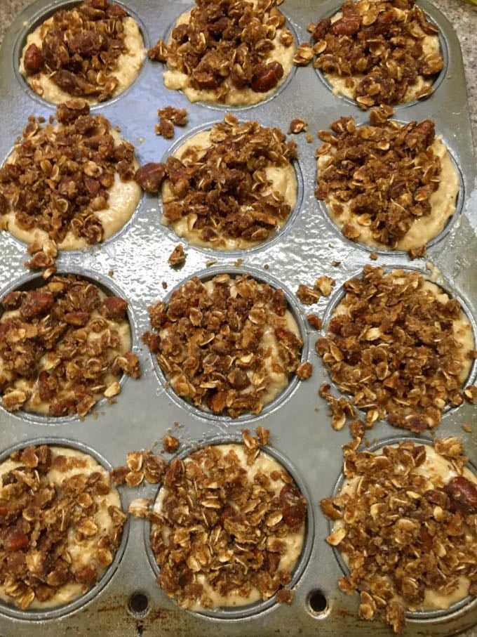 A muffin pan with oatmeal muffin batter and topping filling the cups.