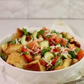 A white serving bowl with a salad with toasted croutons, fresh summer tomatoes and cucumbers.