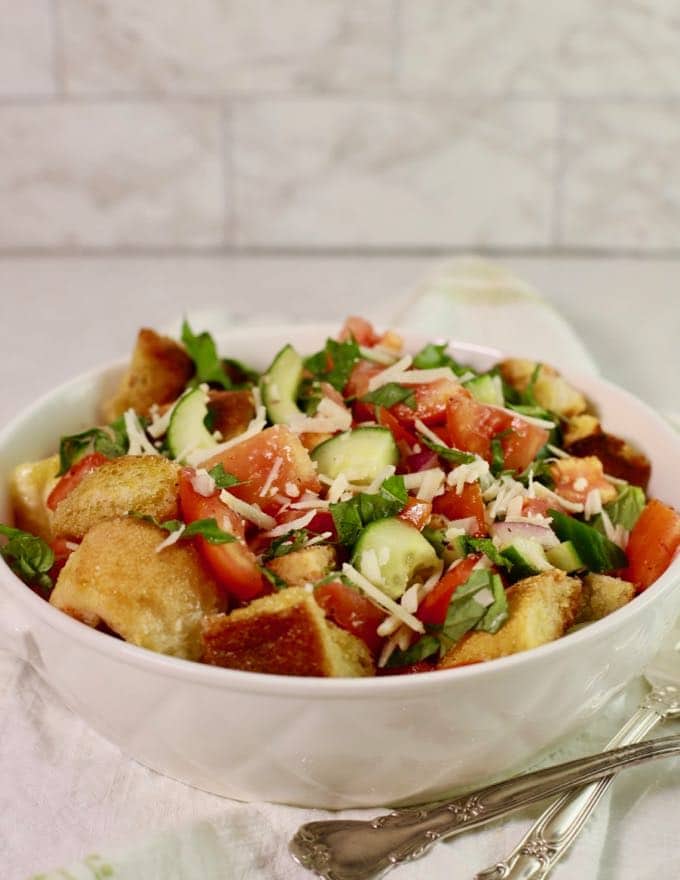 A white serving bowl with a salad with toasted croutons, fresh summer tomatoes and cucumbers.