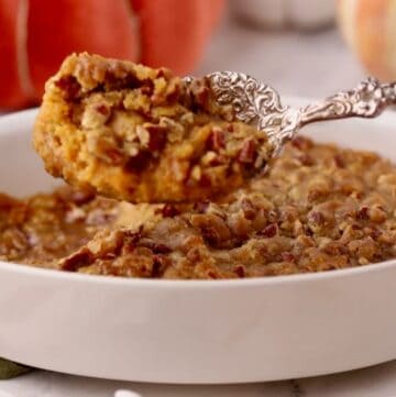 A large spoonful of sweet potato casserole with pecan topping over the casserole dish.