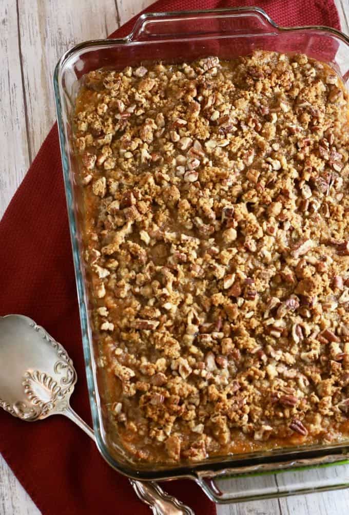 A clear glass baking dish with a sweet potato casserole topped with pecans.