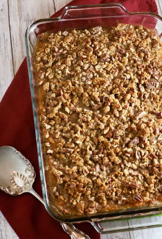 A clear glass baking dish with a sweet potato casserole topped with pecans. 