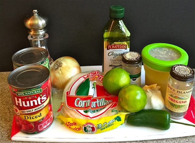 Soup ingredients including canned diced tomatoes, limes, chicken broth, onion and olive oil. 