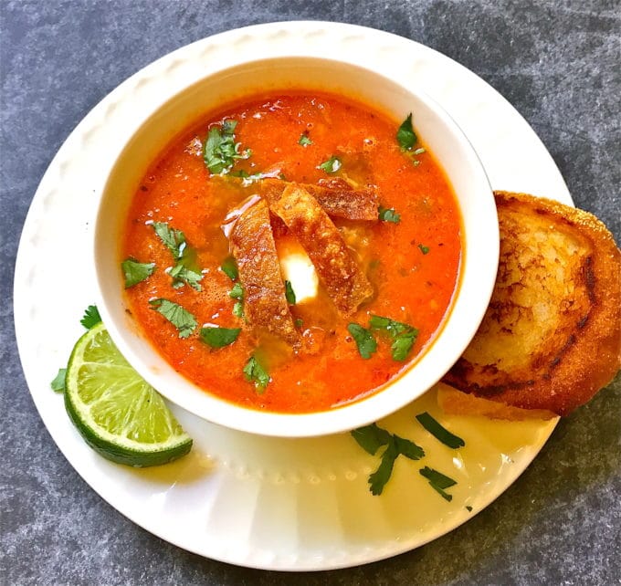 Tomato tortilla soup in a white bowl, with a grilled cheese sandwich. 