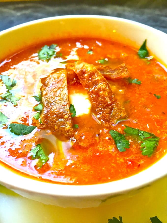 A white bowl with Tomato Tortilla Soup topped with chopped cilantro. 