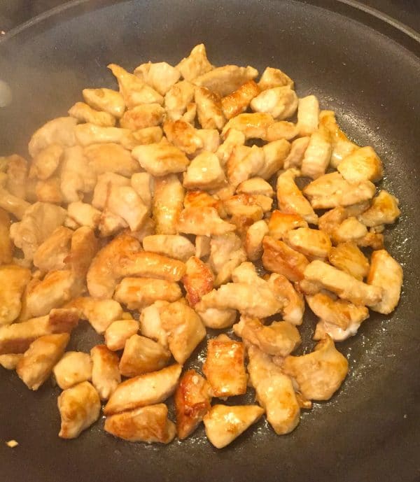 Chunks of chicken cooking in a large skillet.