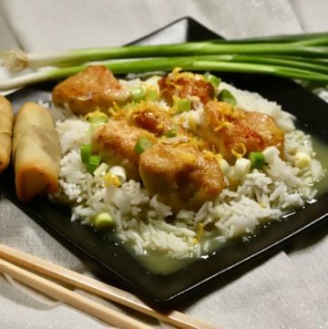 Lemon Curd Chicken on a black plate over rice.